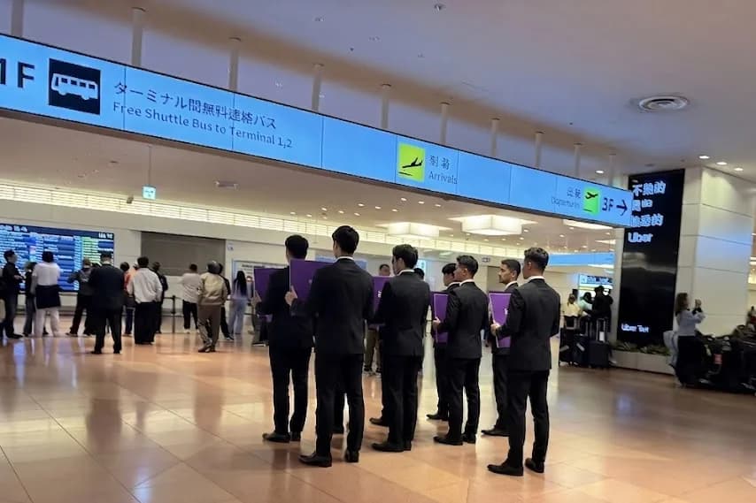 Uniformed chauffeurs holding passenger name boards in a Tokyo airport arrivals hall